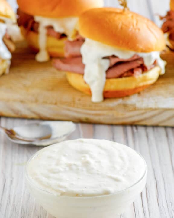 A bowl of copycat Arby's horsey sauce and roast beef sandwiches behind it.